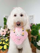 Dog Bandana in pink with bunny design on a happy dog, surrounded by flowers and greenery.