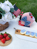 Patriotic picnic scene with dog bandana, Coca-Cola bottles, cookies, strawberries, and American flags.